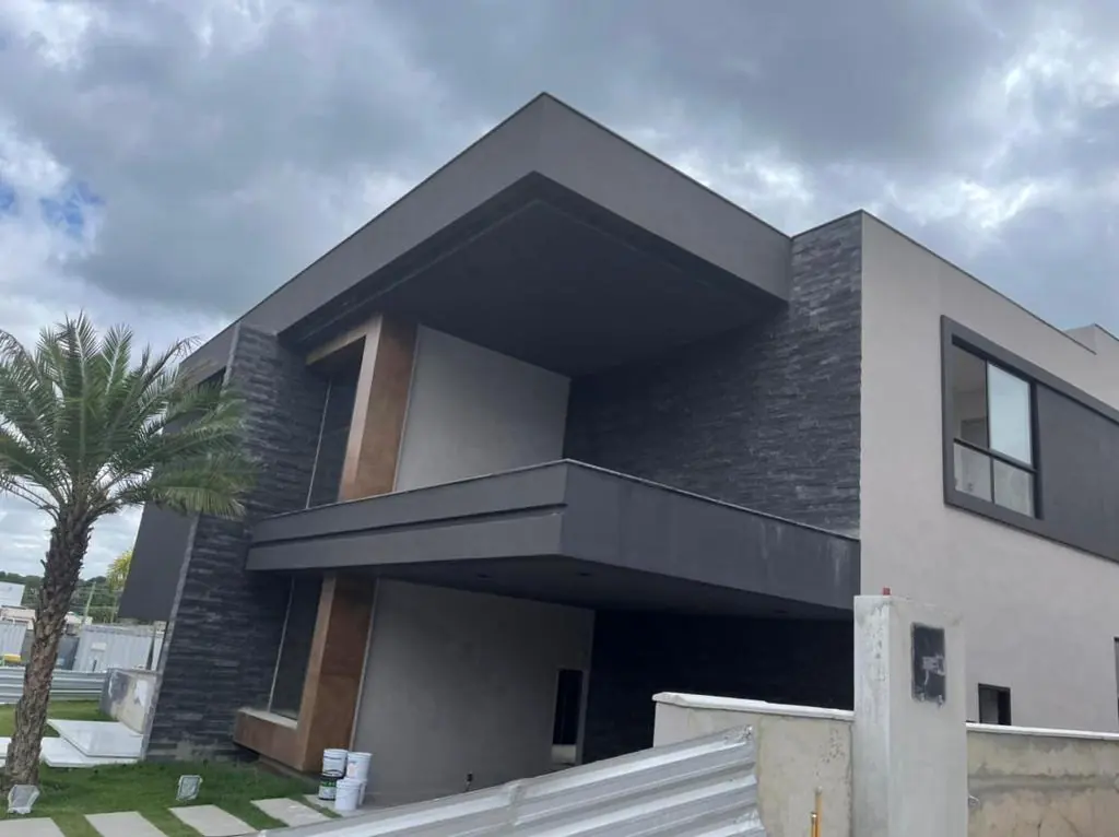 Fachada de residência de alto padrão com volumes em concreto, revestimento em pedra e madeira